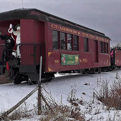 Steam train in snowy landscape with Santa waving from the rear platform.