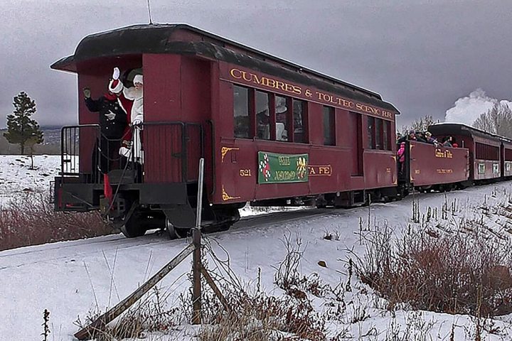 Steam train in snowy landscape with Santa waving from the rear platform.