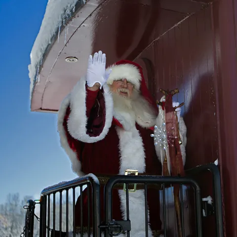 Santa Claus waving from a snowy train caboose in winter.