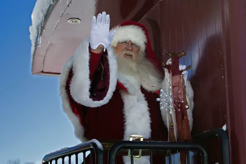 Santa Claus waving from a snowy train caboose in winter.