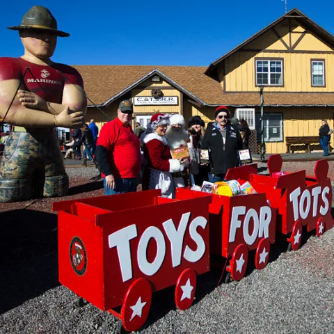 People stand by a 'Toys for Tots' cart and inflatable Marine at a train station.