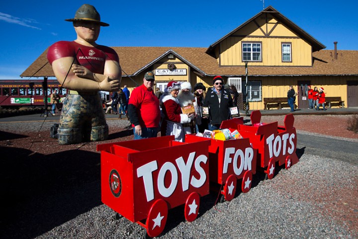 People stand by a 'Toys for Tots' cart and inflatable Marine at a train station.