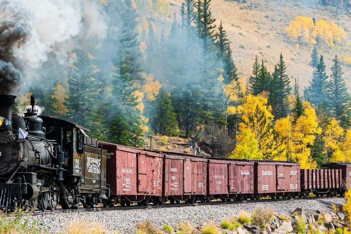 a train on a track with smoke coming out of it with Durango and Silverton Narrow Gauge Railroad in the background