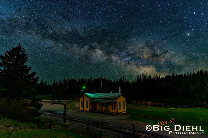 Yellow cabin under a starry night sky with the Milky Way visible in a forested area.
