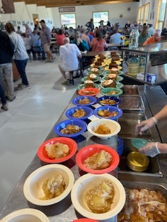 Osier cafeteria with colorful bowls of dessert lined up, busy with people seated in the background.