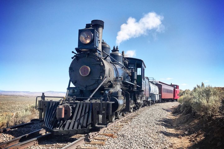 Engine 168 steam train with black engine and red carriages on a sunny day on tracks in a rural landscape.