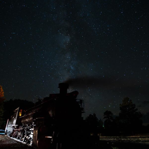 Silhouetted steam train under a starry night sky with Milky Way visible.