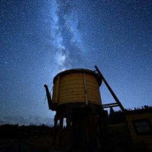 Silhouette of old water tower under starry Milky Way sky.