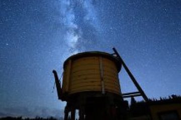 Silhouette of old water tower under starry Milky Way sky.