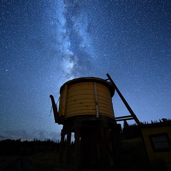 Silhouette of old water tower under starry Milky Way sky.