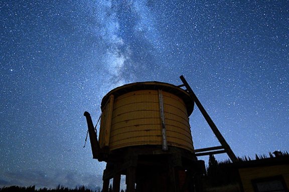 Silhouette of old water tower under starry Milky Way sky.