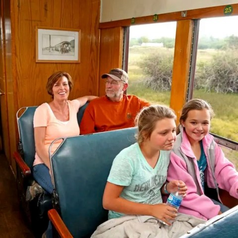 Four people sitting on a train, two adults and two children, looking out the window at the scenery.