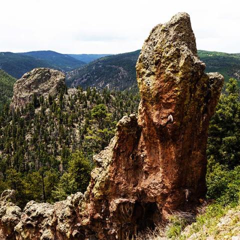 Rock formations and pine forest on a mountain with distant hills.
