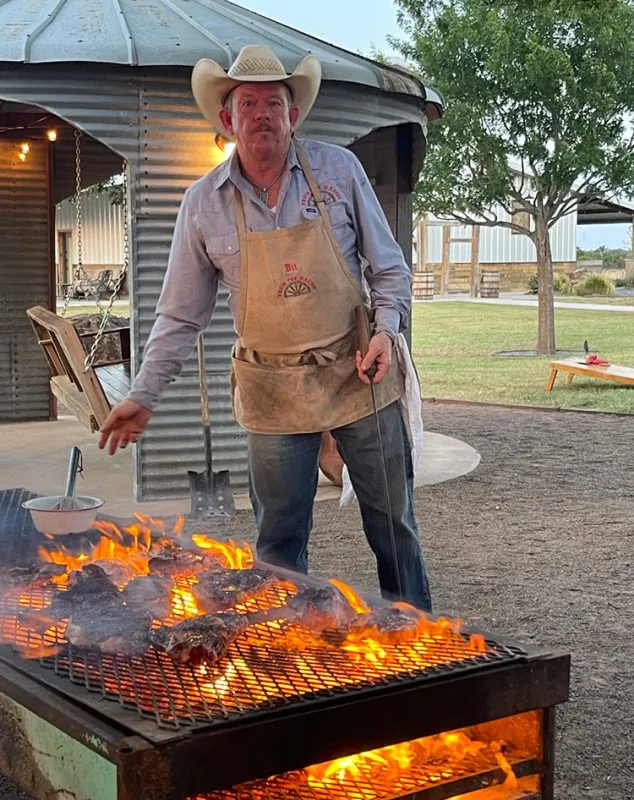Bit Pruitt grilling meat outdoors with flames on a barbecue.