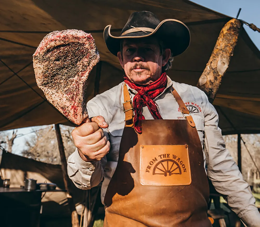 Bit Pruitt holding a seasoned meat cut under a tent.