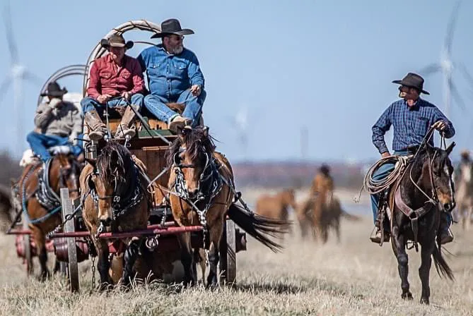 Cowboys on a horse-drawn wagon and horseback in an open field.
