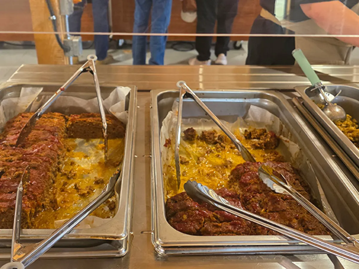 Buffet with trays of meatloaf, curry, and a green serving spoon behind glass.