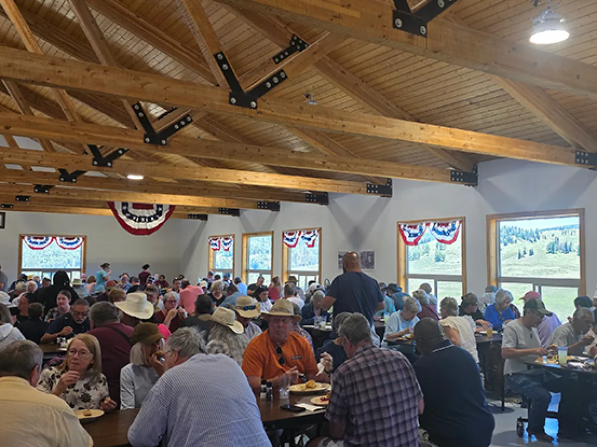 Crowded dining hall with people sitting at tables under wood beam ceiling.