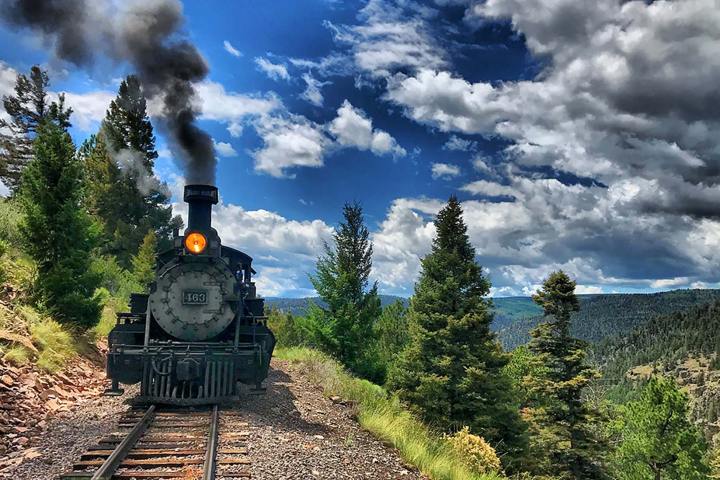 Locomotive 463 on a mountain track with trees and cloudy sky.