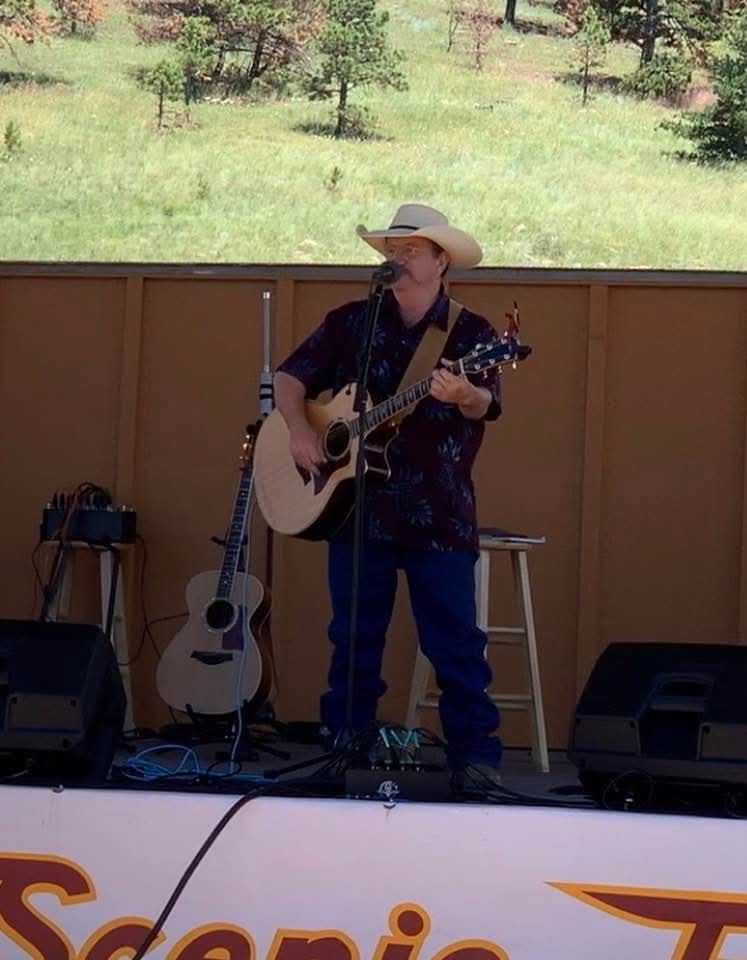 San Luis Valley musician Fred Hargrove in cowboy hat playing guitar on outdoor stage.