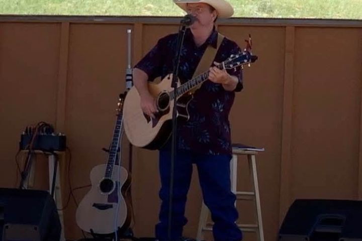 San Luis Valley musician Fred Hargrove in cowboy hat playing guitar on outdoor stage.