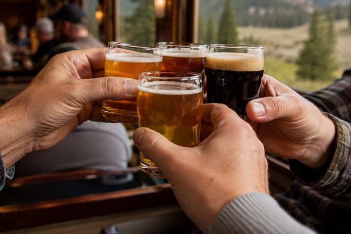 Four hands clinking glasses of beer in a cozy bar setting.