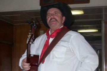 Fred Hargrove with guitar, wearing cowboy hat and red scarf.