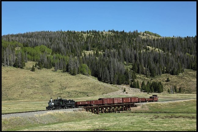Train on bridge in rural landscape with forested hills.