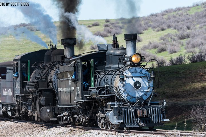 Vintage steam train traveling through countryside on a clear day.