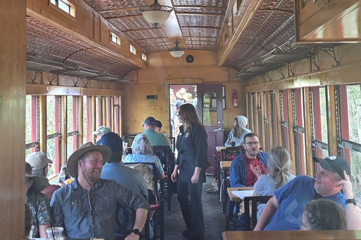 People seated in a vintage train car, with wooden interior and patterned ceiling.