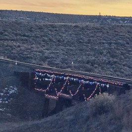 Train bridge with colorful lights in a vast, barren landscape at sunset.
