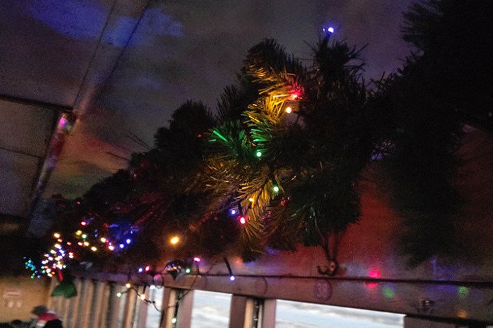 Festive lights and pine garland decorate a train interior.