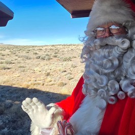 Santa Claus in red suit holding candy canes on a train, waving.