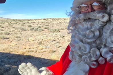 Santa Claus in red suit holding candy canes on a train, waving.