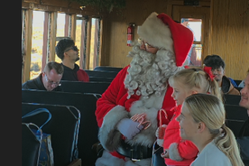 Santa with children on a train, people seated nearby.