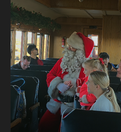 Santa with children on a train, people seated nearby.
