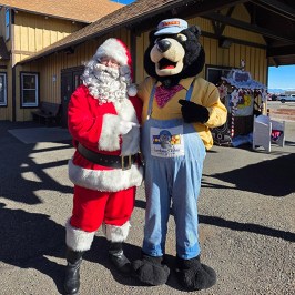 Santa and bear mascot in costume stand outside a building.