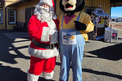 Santa and bear mascot in costume stand outside a building.