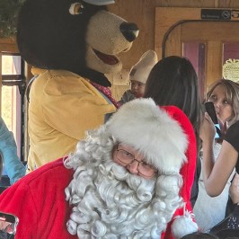 Santa and bear mascot interacting with children on a train.