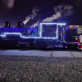 Steam train with festive lights and Santa Claus at night.