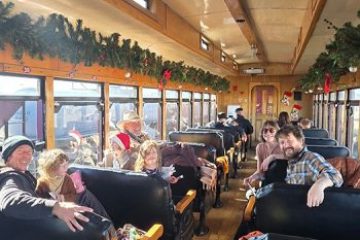 People in festive train car with holiday garlands on windows.