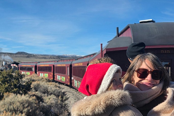 Woman and child in winter clothes near a red train in a desert landscape.